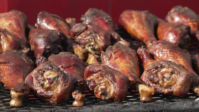 This close up video shows a panning view of large turkey drumsticks cooking on an outdoor fire grill. 