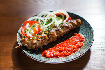 grilled kebab with rich tomato sauce and onion rings served on plate on wooden background