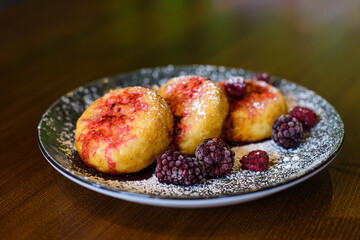 cheese pancakes with raspberry and blackberry filling and powdered sugar on plate on brown wooden background