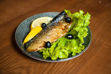 oven cooked mackerel in mustard with lettuce and lemon slice on plate on wooden table background
