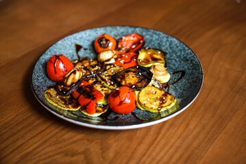 grilled zucchini and tomatoes with rich barbecue sauce on plate on wooden table background