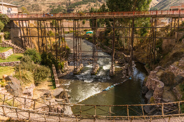 river near stone construction and metal bridge in checacupe, cusco, peru