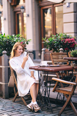 Beautiful woman drinks coffee in a cozy cafe on a city street.  People, fashion,  lifestyle, travel and vacations concept