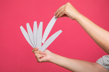 Set of nail files in woman hand and choosing one of them on pink background. Manicurist equipment - obrazy, fototapety, plakaty