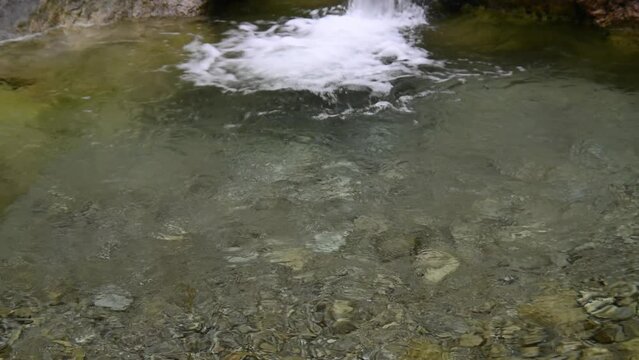 Sehr sauberes Wasser pl&auml;tschert in ein Becken eines Bergbachs. Am Grunde des Beckens sind sch&ouml;ne Steine.