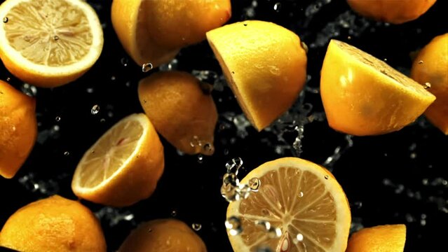 Halves of fresh lemons with drops of water fly up and rotate in flight. On a black background. Filmed on a high-speed camera at 1000 fps.