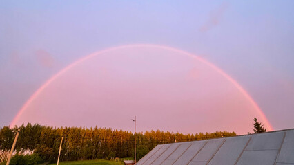 a full rainbow from the roof of the house over the forest and houses. Double Rainbow