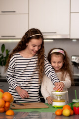 Two cute sister girls are making orange fresh juice. They are in the kitchen at home. Family. Fresh fruit. Healthy eating.
