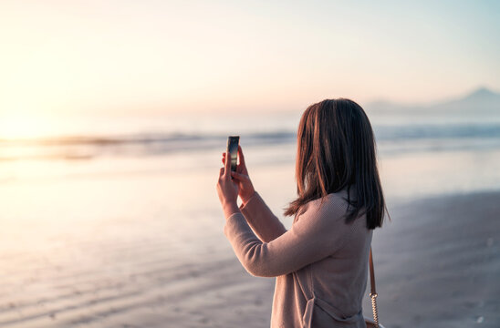 silhouette of a woman on the beach at sunset taking pictures with smartphone