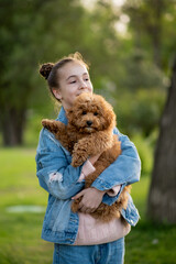 A cute teen girl on a walk with toy poodle dog. It's spring outside. The girl is dressed in a blue jacket in a flower and jeans. Childhood. Pets.