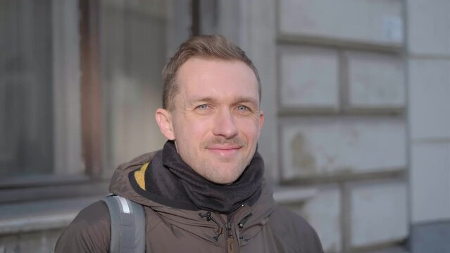 Happy smiling male hipster person with mustache staying outdoor looking at camera. Businessman wearing casual wear in the morning at the street. Freelancer concept. High quality 4k video