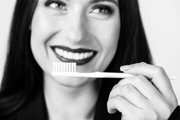 Obraz premium Healthcare and medicine concept. Close-up studio shot of woman holding white toothbrush in front of her mouth with white teeth and red lips. White toothbrush is in camera focus