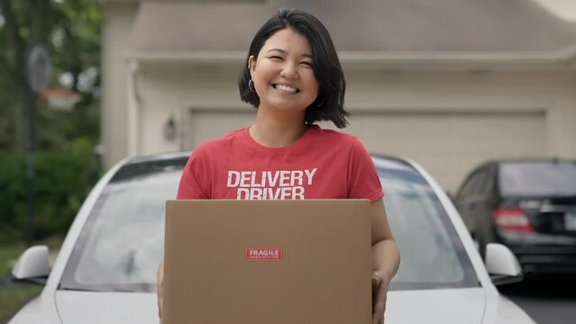 Delivery driver Asian woman holding package box and looking at camera. Slow motion
