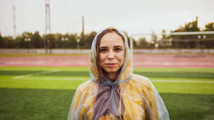 Young woman in raincoat in rainy weather. Portrait of positive female in wet waterproof coat.