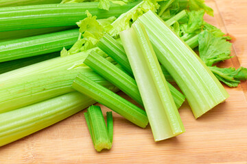 Fototapeta premium Fresh Celery Stem and Chopped Celery Sticks on Wooden Cutting Board. Vegan and Vegetarian Culture. Raw Food. Healthy Diet with Negative Calorie Content. Slimming Food