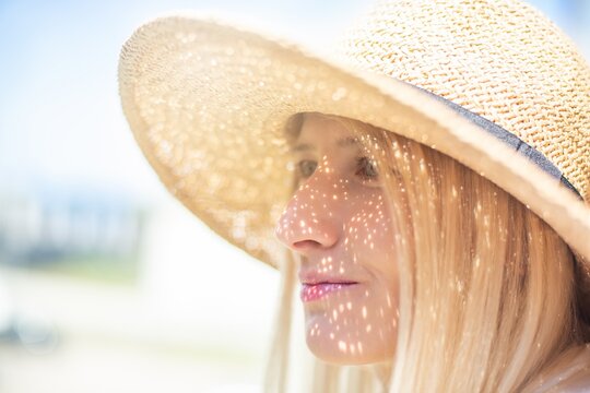 Beautiful blond woman in a straw hat. The sun's rays on her face