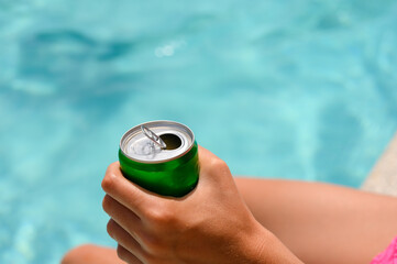 Close-up of an open can of a drink in a hand against the backdrop of a swimming pool. Selective...