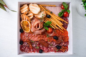 catering box with salami, prosciutto, bacon and breadsticks