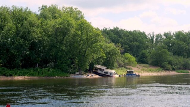 A pontoon boat is tiied up to an abandoned houseboat along shore of Mississippi River.