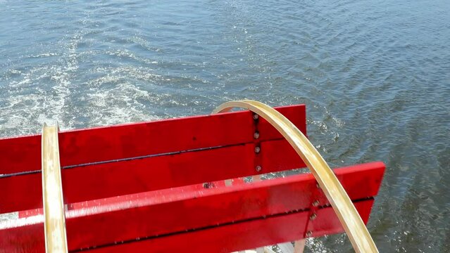 Rotating red paddle wheel of a cruise boat in motion on the water, in closeup handleld clip.