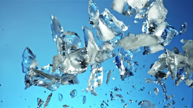 Pieces of ice with splashes of water soar up and fall. On a blue background. Filmed is slow motion 1000 fps.