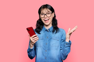 Naklejka premium Surprised teenage girl looking at smartphone screen on pink background