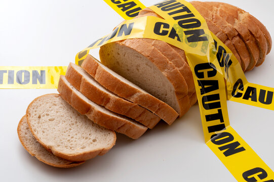 Sliced bread and yellow caution tape isolated on white background concept for food insecurity, hunger warning and hazardous processed grain