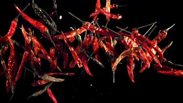 Pods of dried chili peppers fly up and fall down. On a black background. Filmed on a high-speed camera at 1000 fps. 