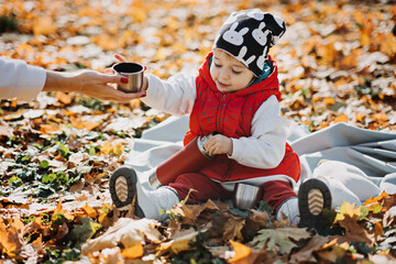 Happy little toddler baby daughter with red thermos and cup in autumn picnic in fall nature background