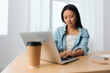 Focused serious young Asian cute female businesswoman type tax report on laptop in light office interior. Employee freelancer work at home. Lady corporation leader concept. Copy space Banner Offer