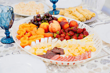 cheese and meat cuts and fruit in a large white plate on the festive table. 