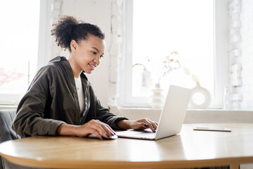 Fototapeta premium Female student uses laptop computer workplace in coworking space, online learning, working with documents