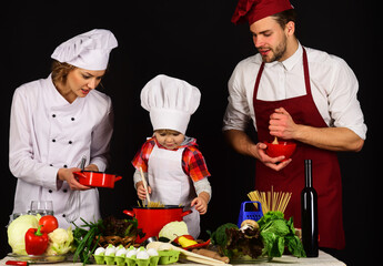 Child with parents cooking at kitchen. Happy family in chef uniform preparing dinner together.