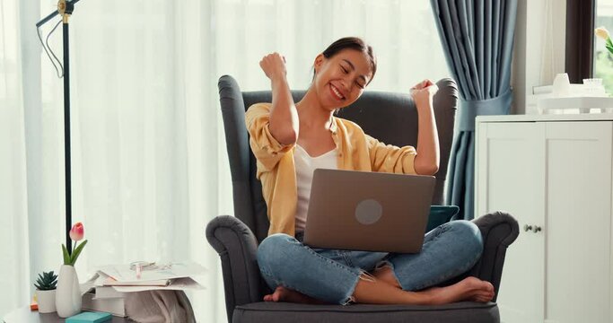 Young asia female girl or university student sit on sofa chair with laptop feel happy enjoy dance done her job, finish work report in living room at home. Work from home, Work life balance concept.