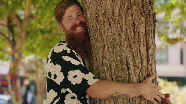 Young redhead man smiling confident hugging tree at park