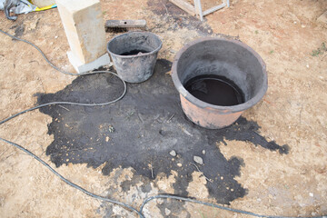  dirty bucket of oil standing in a black puddle near a construction site