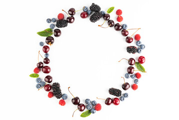 Cherries, blueberries, blackberries, raspberries and mint leaves are arranged in a circle on a white background. View from above.
