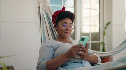 African american woman using smartphone lying on hammock at home terrace