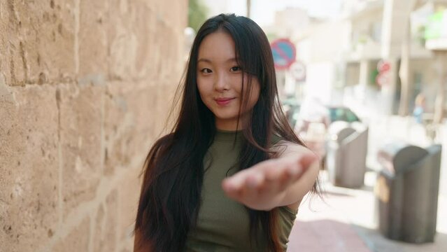 Young chinese woman smiling confident doing coming gesture with hand at street