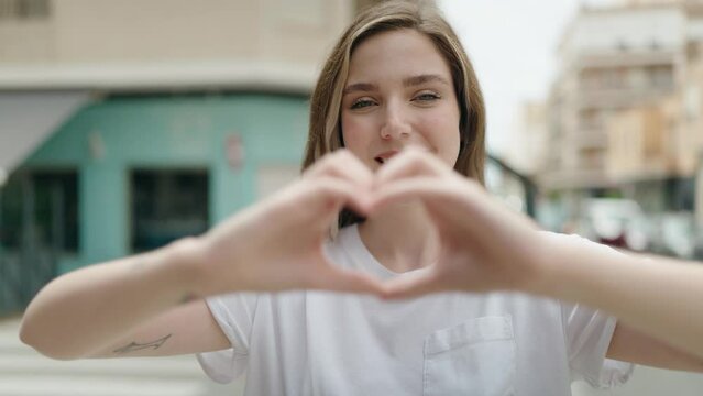 Young woman smiling confident doing heart gesture with hands at street