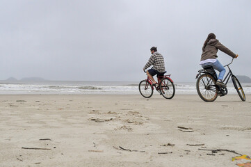 Obraz premium Young couple cycling on a beach on Honey Island (Ilha do Mel) in a cloudy day