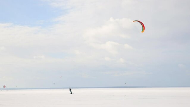 Minimalism scenic view of adult man enjoy extreme sport activities riding kite surfing board on white desert snow frozen lake surface against blue sky. Winter outdoors adventure lifestyle