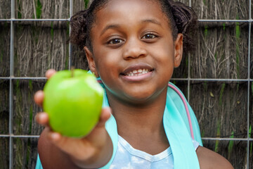 afroamerican school girl with backpack, eating green apple. Daily rate of fruit for children.