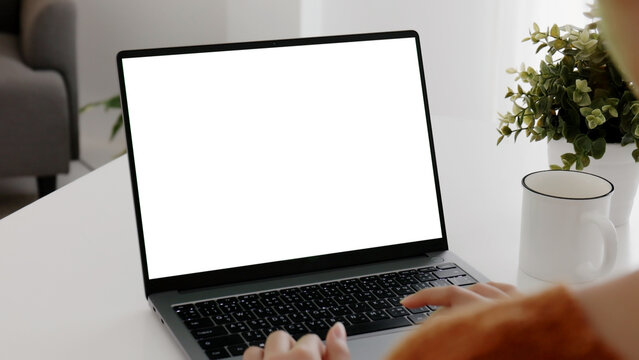 Young Asian woman using laptop computer at home with white blank monitor screen.