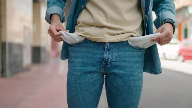 Young hispanic man showing empty pockets at street