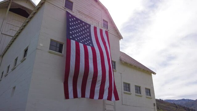 Slow tilt up on majestic American flag draped on rustic barn with sun flare