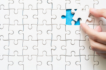 Close up hand holding and playing jigsaw game incomplete. White part of jigsaw puzzle pieces on...