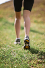 Closeup photo of athlete girl's legs dressed in sportswear with sneakers going up in mountains on summer green grass. Happy young female sport, workout, travelling, ecology, healthy lifestyle concept