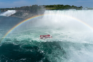 Niagara Falls, ON, Canada - June 30, 2022: Rainbow over the falls with Maid of the Mist Boat in the river in Niagara Falls, Ontario, Canada
