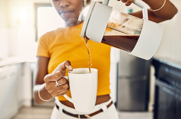 Hands of woman pouring coffee into a mug, standing inside a kitchen at home. French press with...